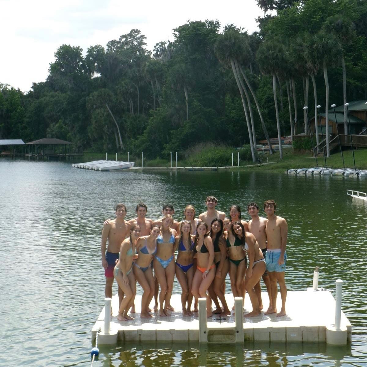 A large group of friends standing on a floating dock at a wooded lake