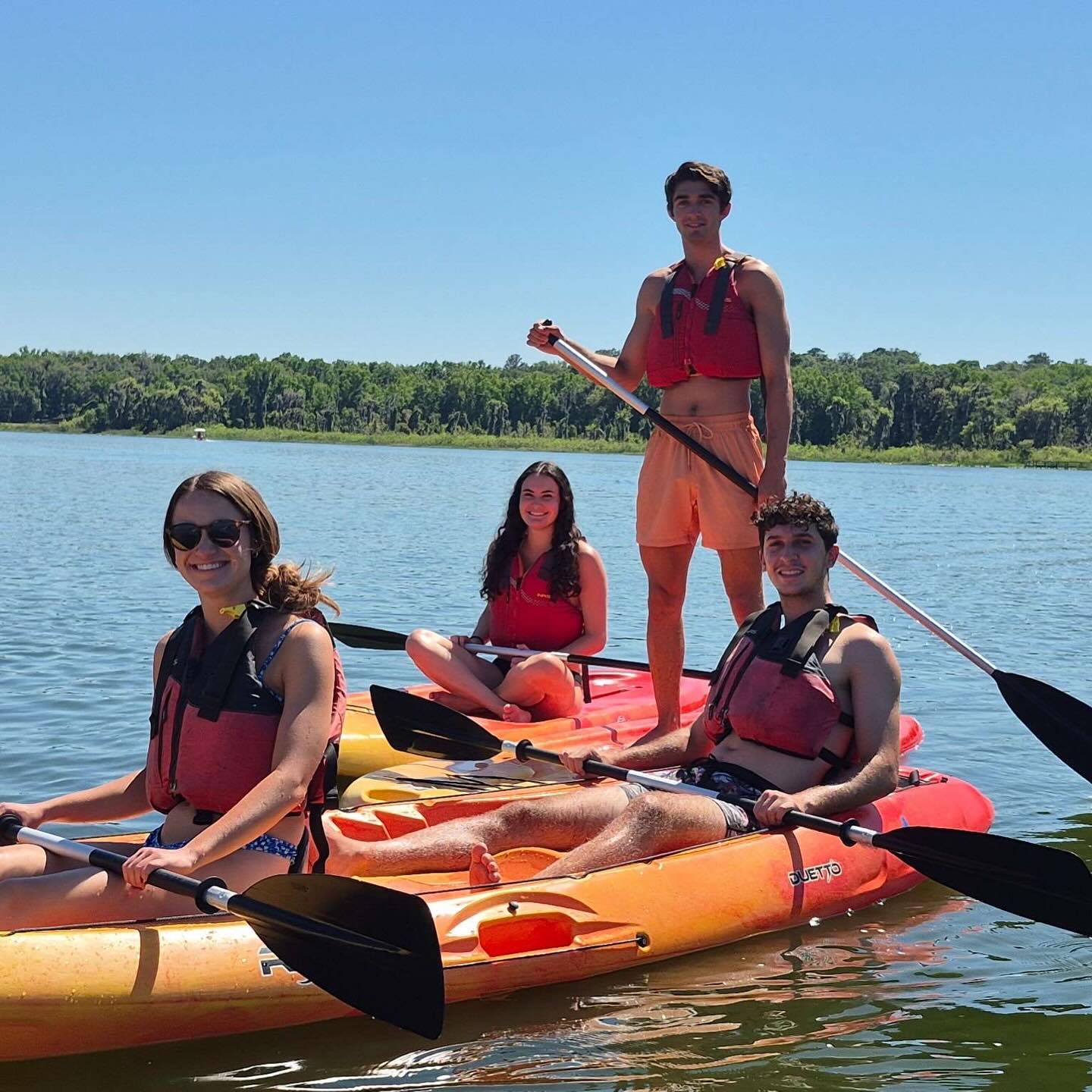Rafael and friends in life vests on kayaks and a paddleboard on a lake