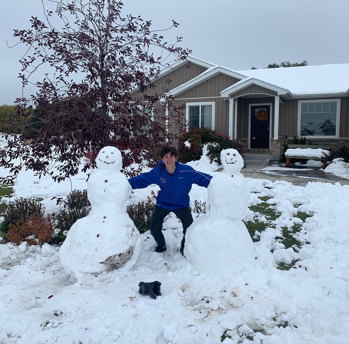 Rafael standing outdoors in the snow between two snowmen in Idaho